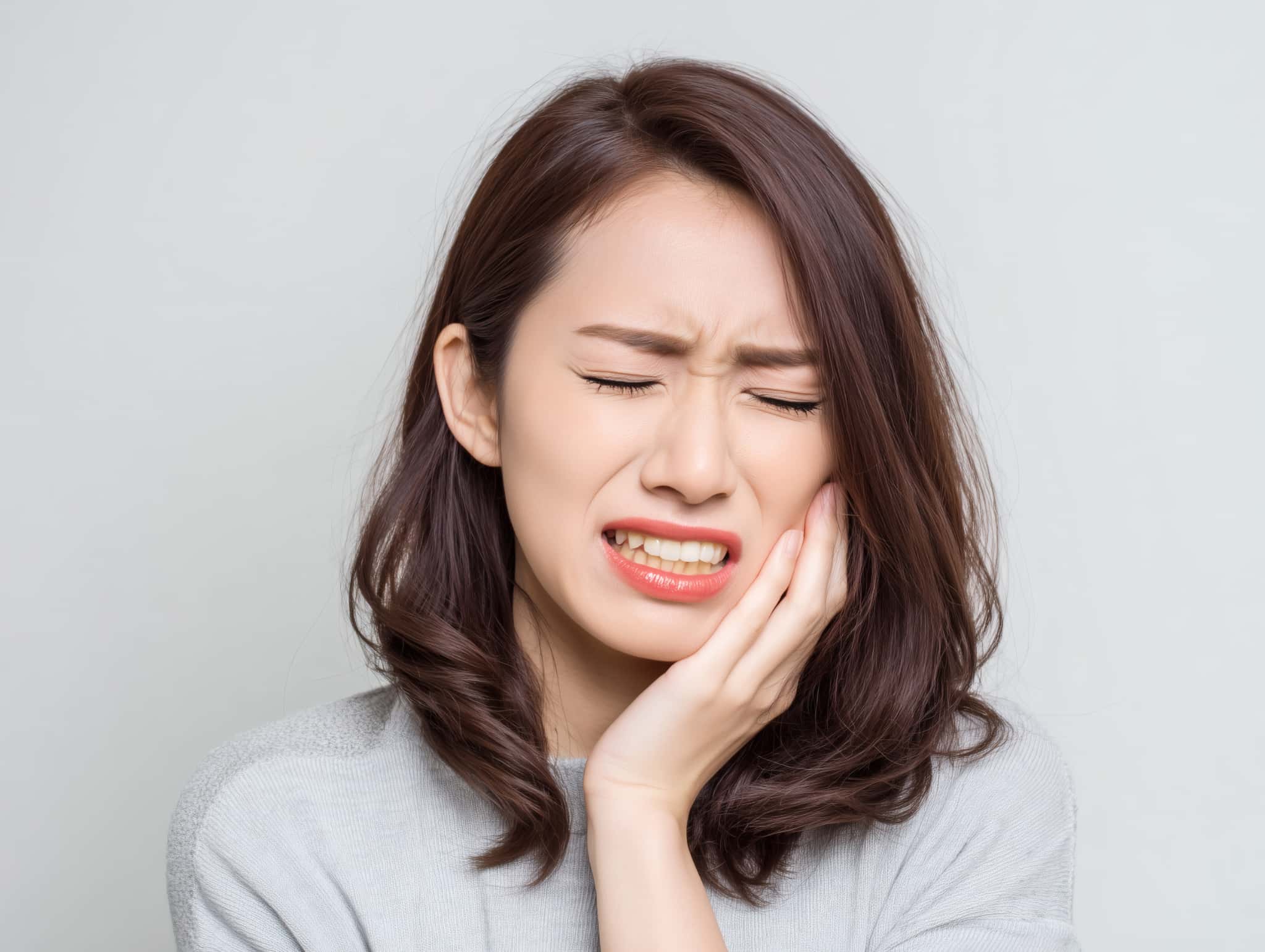 虫歯が痛んで顔をしかめて頬をおさえる女性